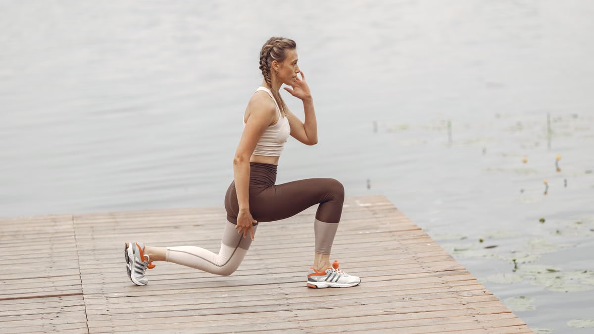 A woman performs lunges on a lakeside wooden deck, showcasing a fit lifestyle outdoors.